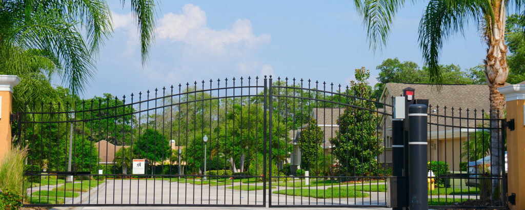 Entrance gate to a beautiful gated residential house community with lush green trees and grass