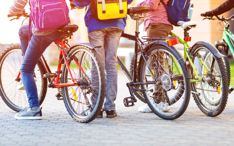 Children with rucksacks riding on bikes in the park near school.